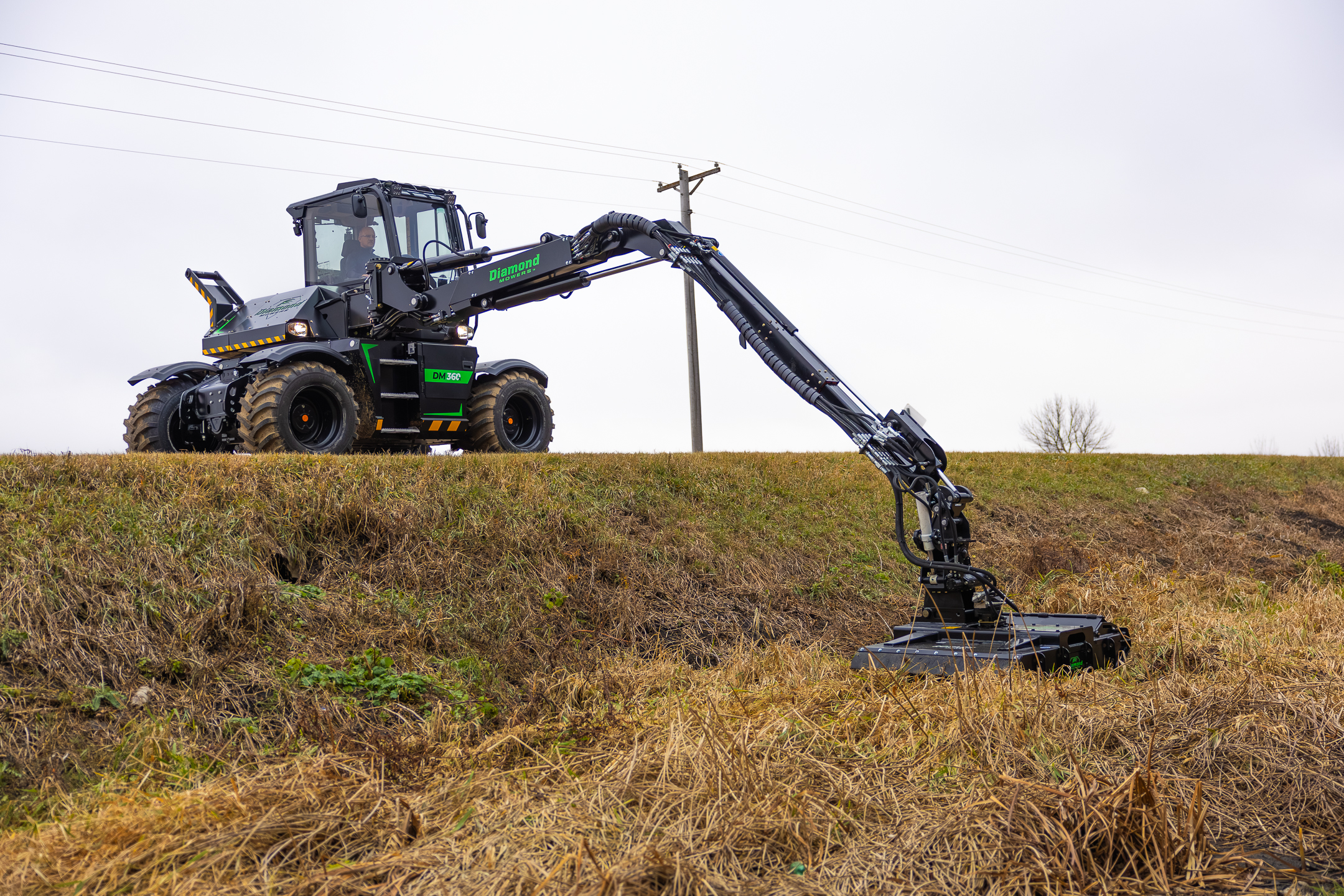 Black and green telescopic handler with extended boom operating in harvested field near power lines