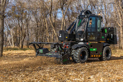 Black and green self-propelled wood chipper operating in a wooded area with bare trees