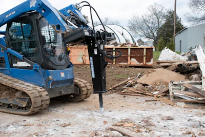 Blue skid steer loader with hydraulic jackhammer attachment at demolition site with debris