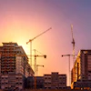 Construction site at sunset with multiple cranes and high-rise buildings under development