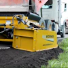 Yellow Widener asphalt paver machine laying dark asphalt on a road with construction trucks in background