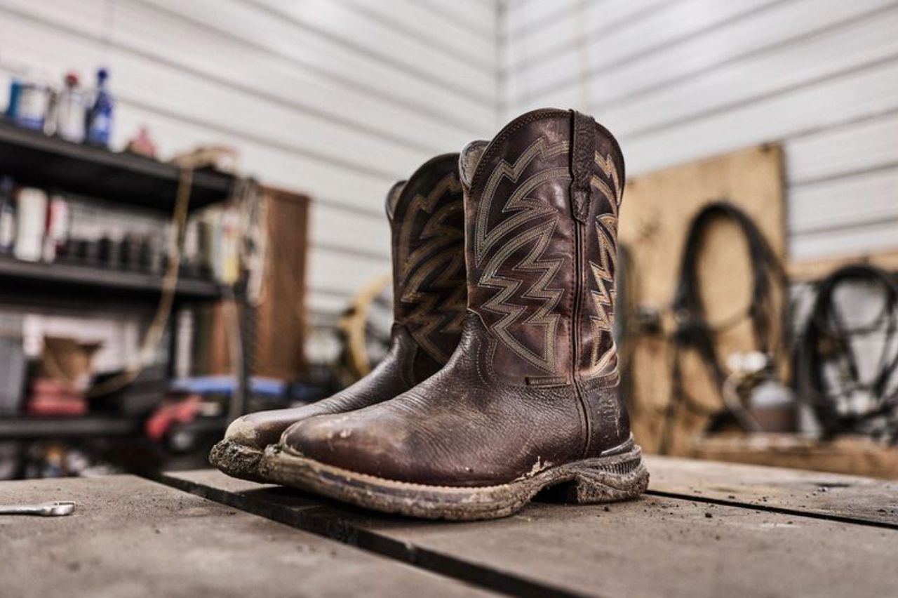 Worn brown cowboy boots with decorative stitching displayed on concrete floor in garage workshop