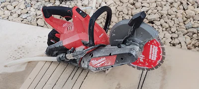 Milwaukee concrete cutting saw with red and black housing on concrete surface with gravel background