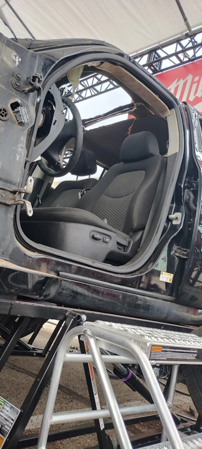 Open car door showing black steering wheel and gray fabric seats on transport trailer