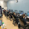 Gaming facility with multiple players seated at computer workstations in a light-filled room with blue-tiled walls