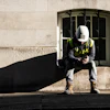 Construction worker in safety gear sitting against stone building wall in sunlight