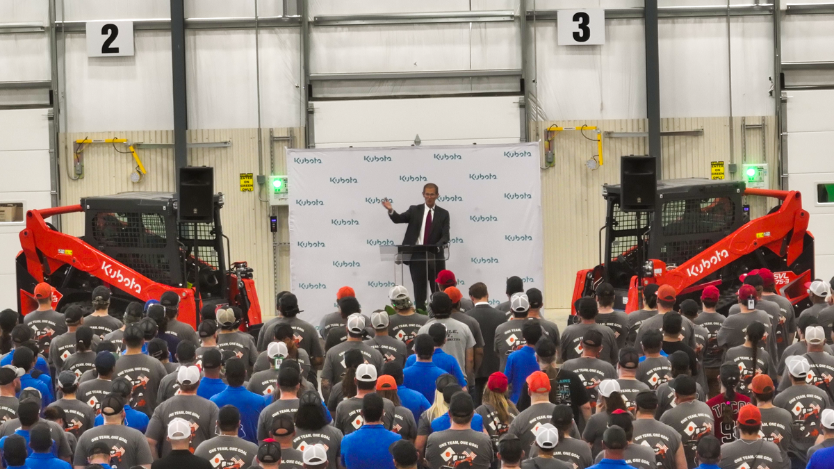 Kubota corporate event with speaker addressing large crowd in industrial warehouse setting with branded machinery