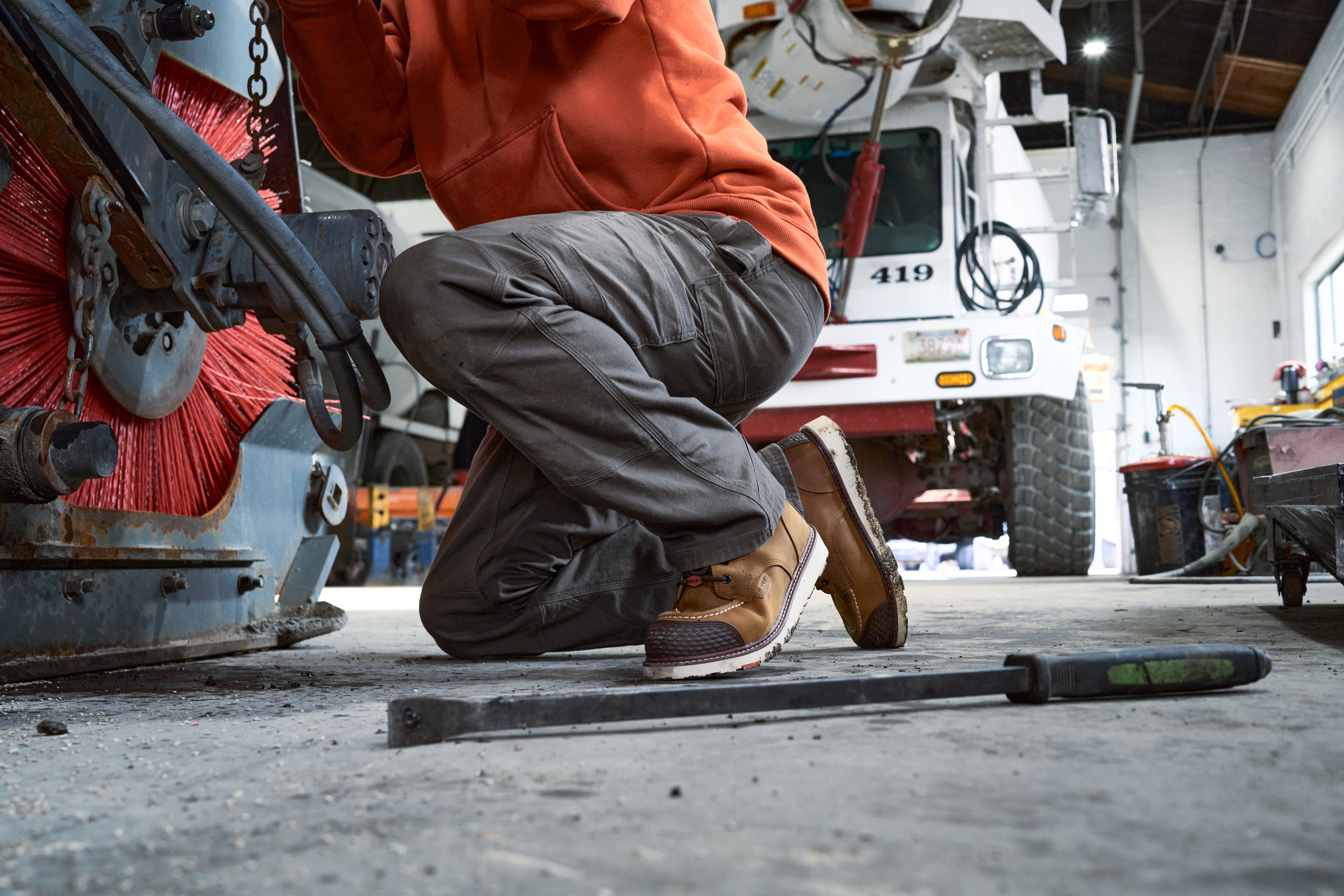 Mechanic crouching while working on equipment in a garage workshop with a fire truck visible in background