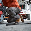Mechanic crouching while working on equipment in a garage workshop with a fire truck visible in background