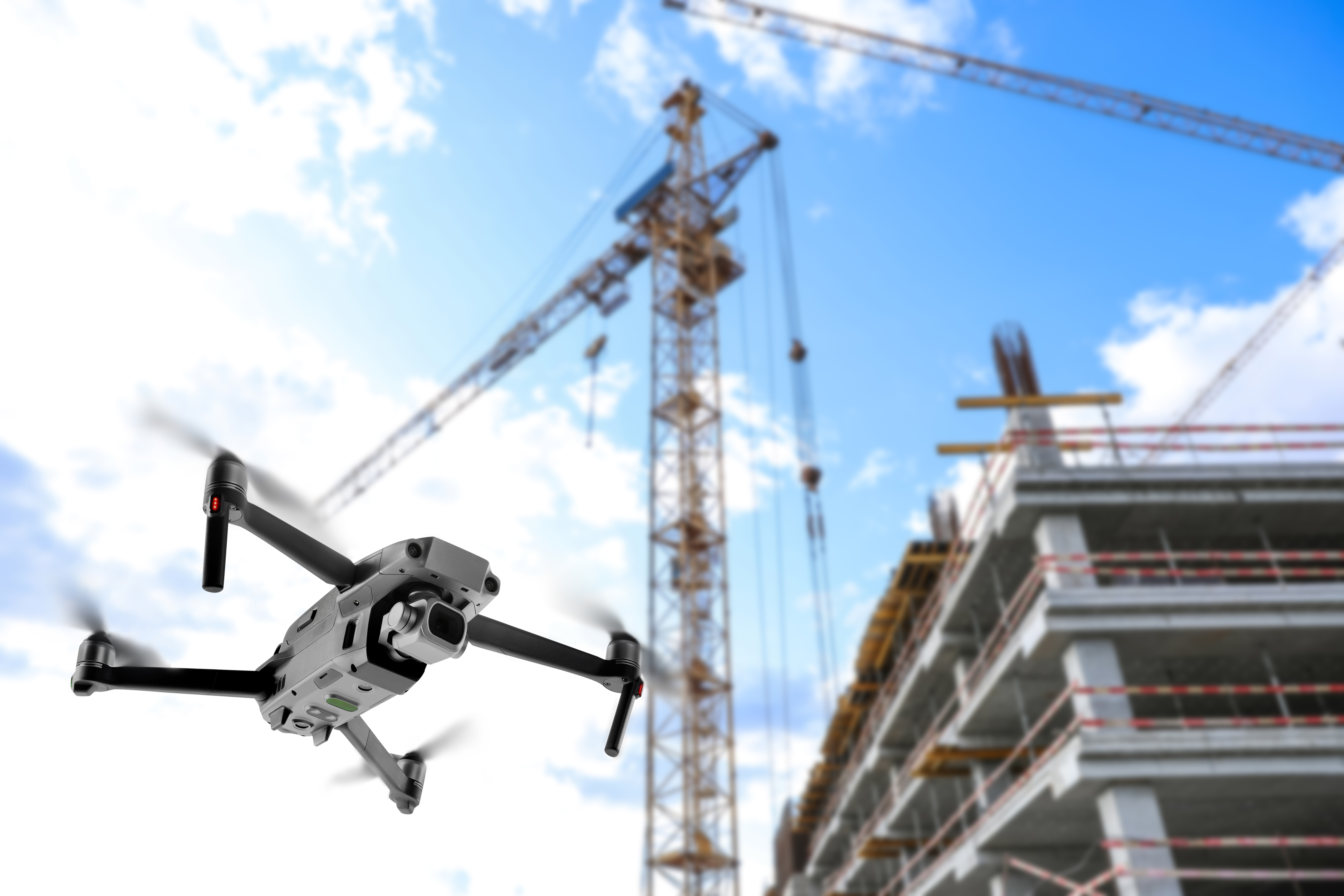 Drone flying over construction site with tower crane and partially built residential building against blue sky