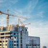 Construction site with multi-story residential buildings under development, featuring yellow tower cranes against a blue sky.