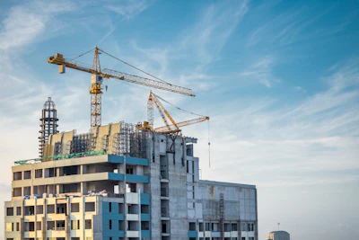 Construction site with multi-story residential buildings under development, featuring yellow tower cranes against a blue sky.