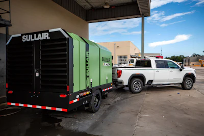 Sullair electric air compressor trailer with green and black exterior parked beside white pickup truck at industrial facility