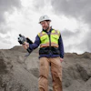Construction worker in safety gear holding thermal imaging camera on gravel site