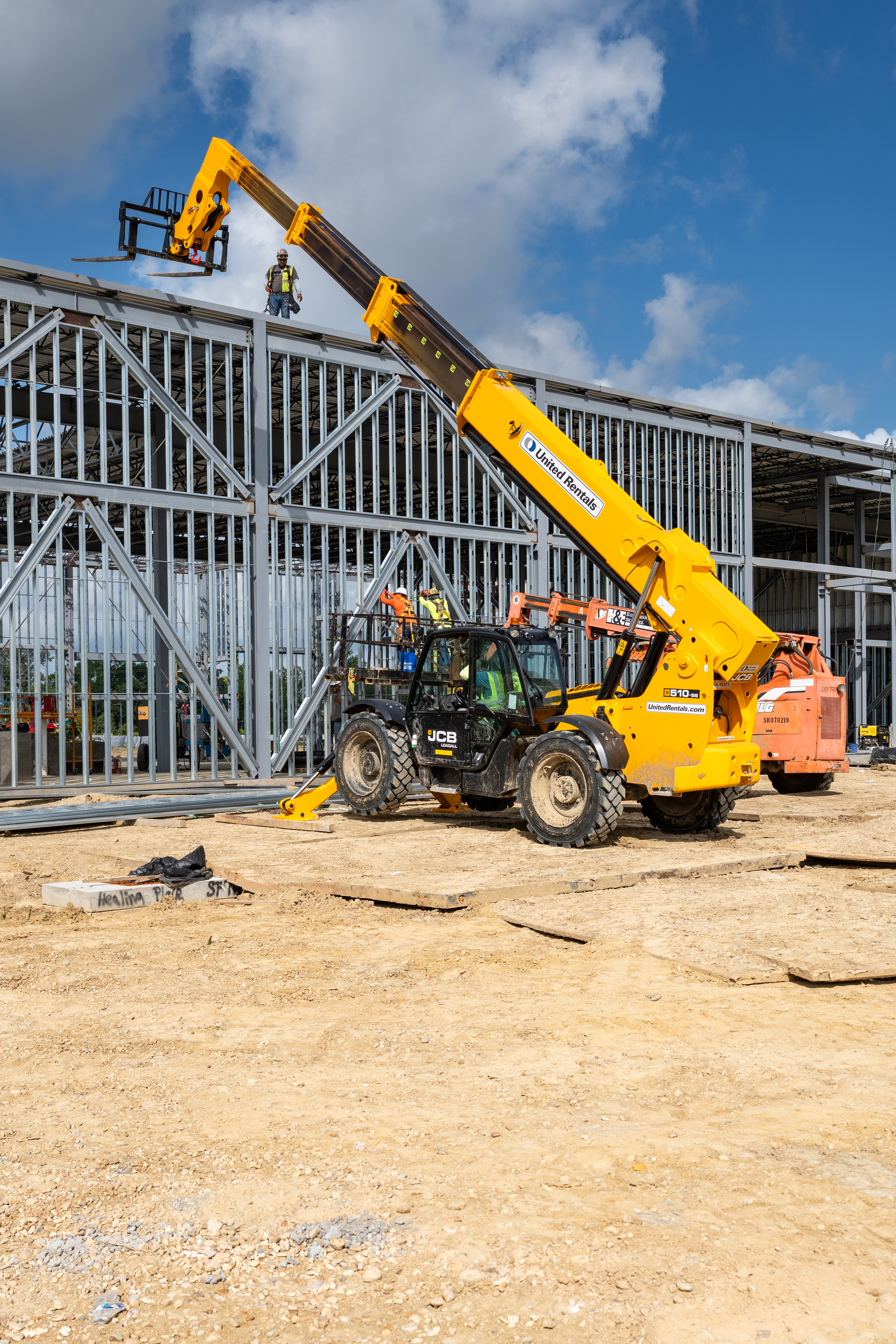 Yellow Liebherr telehandler lifting materials at construction site with metal framework building