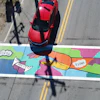 Colorful street mural with comic-style graphics and vibrant colors on urban crosswalk, with red car above