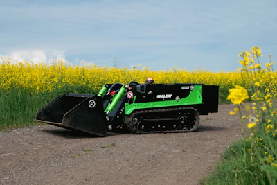 Green and black tracked mini loader positioned on a rural road with yellow rapeseed field in background