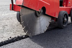 Red asphalt cutting machine with circular saw blade cutting through road pavement