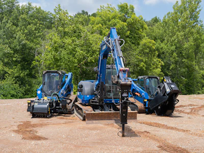 Blue construction equipment including excavator and skid steer loaders positioned at a dirt job site with trees in background