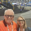 Two people smiling at an industrial trade show with machinery and equipment visible in the background