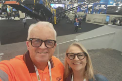 Two people smiling at an industrial trade show with machinery and equipment visible in the background