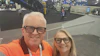 Two people smiling at an industrial trade show with machinery and equipment visible in the background