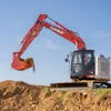 Red Link-Belt excavator with extended boom and bucket digging into dirt pile under blue sky