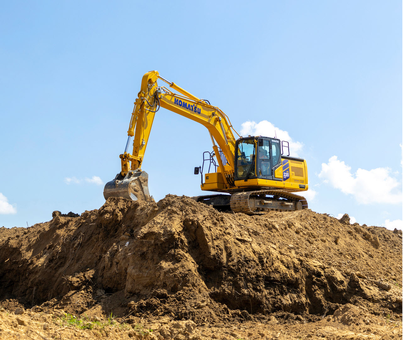 Yellow Komatsu excavator digging earth on construction site under blue sky with white clouds