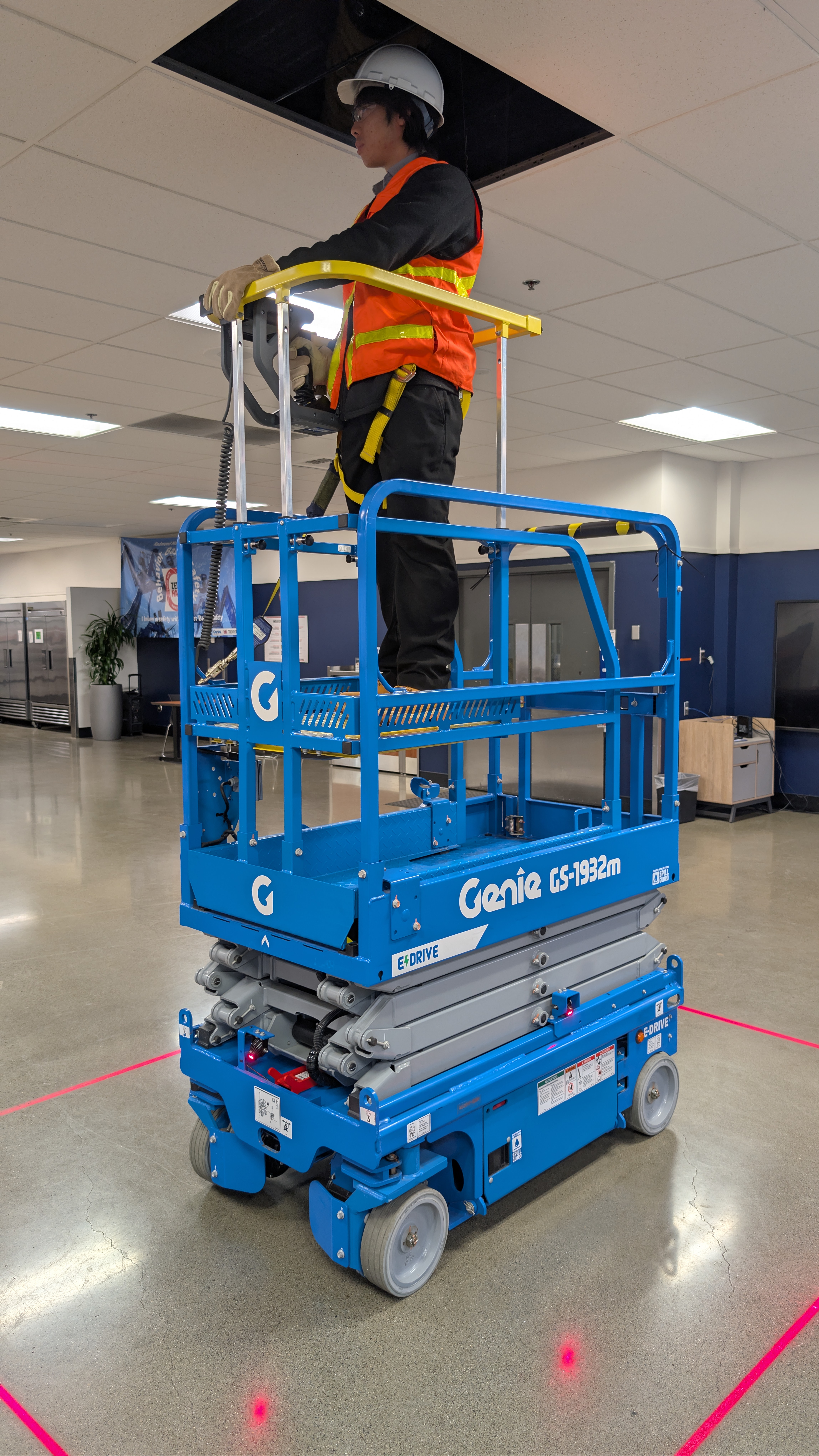 Worker in safety gear operating blue Genie GS-1932m scissor lift indoors