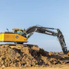 Yellow John Deere excavator on a dirt pile against a clear blue sky