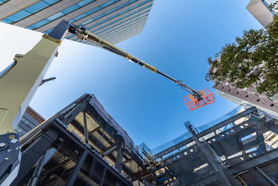Construction crane lifting red safety basket above steel framework and solar panels on clear day