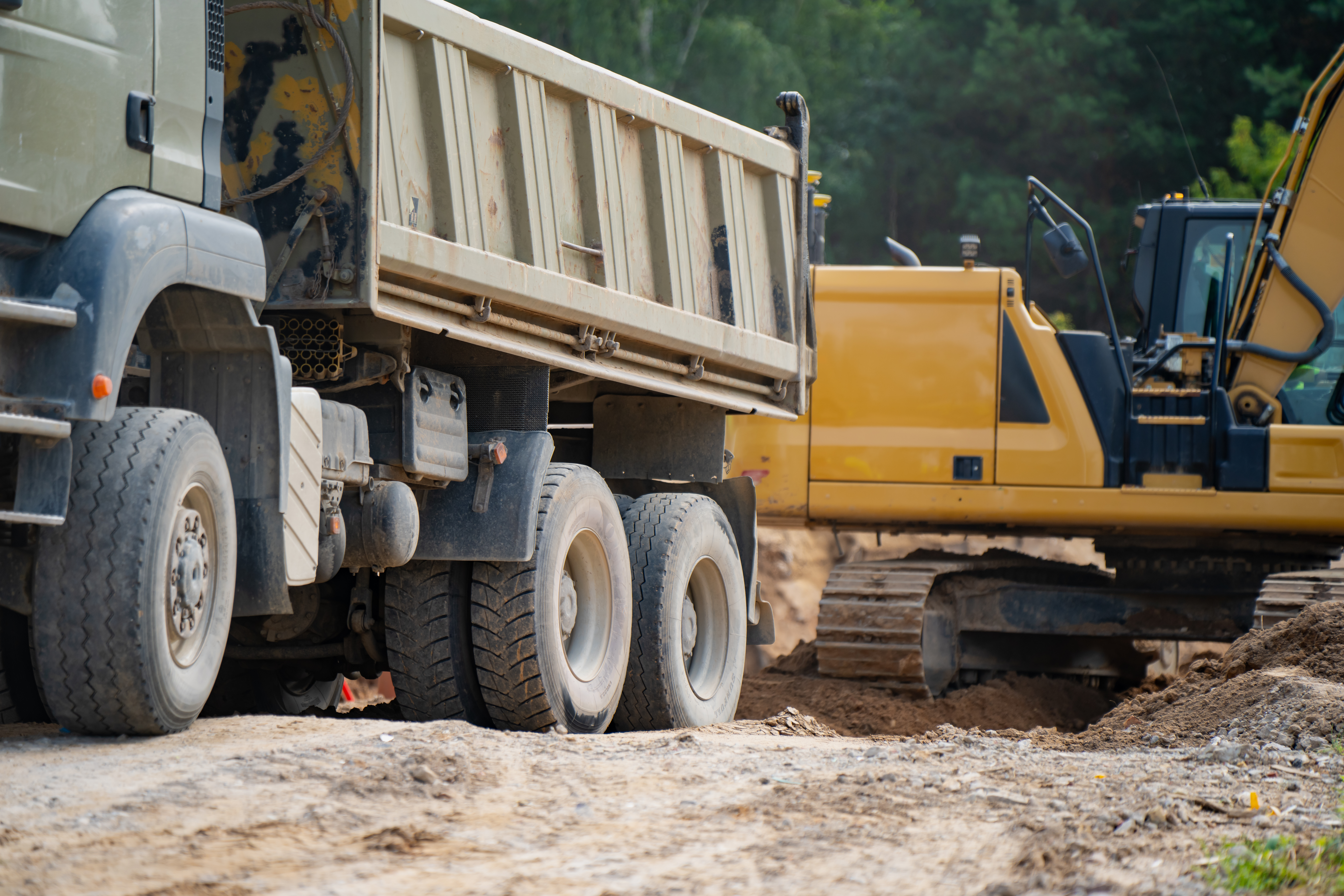 Construction site with white dump truck and yellow excavator on dirt ground
