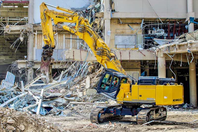 Yellow Kobelco excavator demolishing concrete building structure at construction site