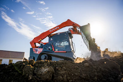 Kubota red and blue skid steer loader moving soil and debris on a construction site under clear sky
