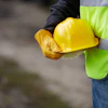 Construction worker holding yellow hard hat wearing neon safety vest and brown gloves