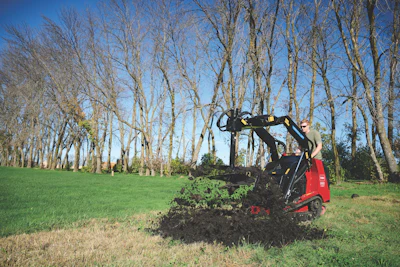 Red wood chipper machine processing branches in a tree-lined park with green grass