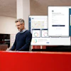 Professional man at red desk reviewing analytics dashboards and software interfaces on multiple computer monitors