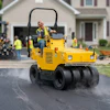 Yellow SAKAI road roller compactor operating on asphalt driveway during residential construction with crew and equipment in background