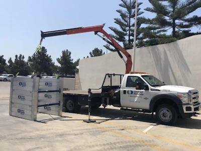 White United Rentals boom lift truck with red hydraulic arm positioned next to stacked equipment pallets in outdoor industrial lot