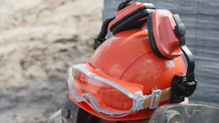 Orange safety hard hat with reflective stripes and protective goggles on a tire at a construction site