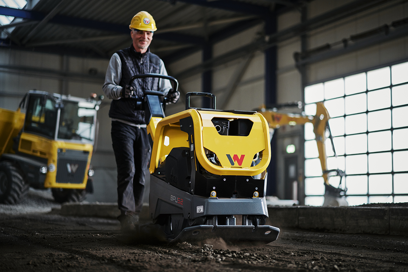 Construction worker operating yellow Wacker Neuson compactor in industrial warehouse setting
