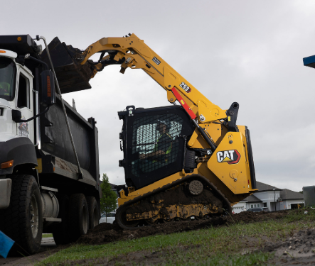 Yellow CAT skid steer loader loading gravel into white dump truck on construction site