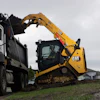 Yellow CAT skid steer loader loading gravel into white dump truck on construction site